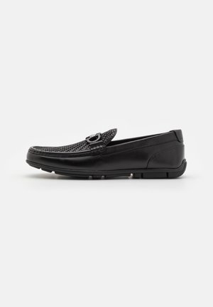 Schwarzer Lederloafer mit gewebtem Obermaterial, Metall-Schnallendetail und Gummisohle, von der linken Seite auf weißem Hintergrund gezeigt.