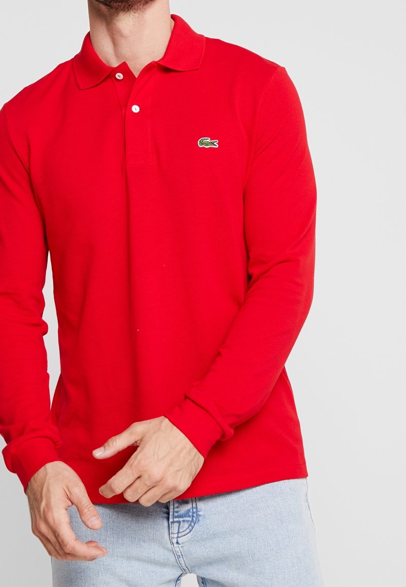 Langarm-Poloshirt aus roter Baumwolle mit klassischem Kragen, Knopfleiste und grünem gesticktem Logo auf der linken Brust.