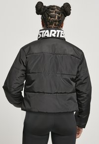 Czarna kurtka puchowa o skróconym kroju, z połyskującą fakturą, poziomym przeszyciem i wysokim kołnierzem z białym logo "STARTER".
