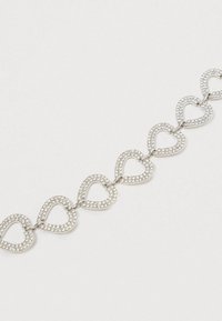 Hõbedane käevõru, millel on omavahel seotud südamekujud, kaunistatud väikeste selgete kristallidega, luues sädeleva efekti.