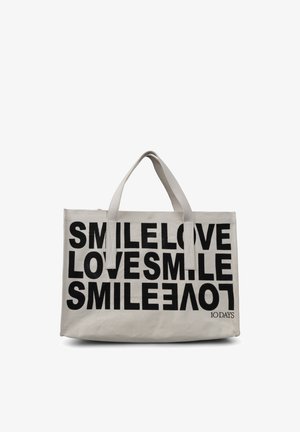 Sac fourre-tout en toile beige clair avec un texte noir audacieux : « SOURIRE AIMER AIMER SOURIRE. » Double poignées supérieures et fermeture éclair.