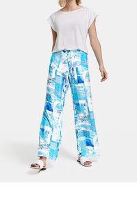 Lätt, lösvit topp i kombination med livfulla blå breda byxor med geometriska och abstrakta mönster. Platta vita sandaler.