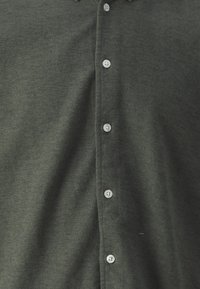 Ciemnozielony materiał z widocznymi guzikami i dziurkami na guziki, ułożonymi w pionowej linii na środku.