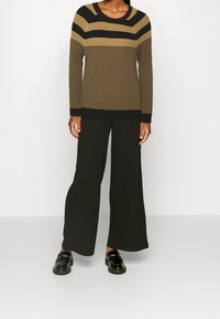 Pull côtelé rayé marron et noir avec un col rond, associé à un pantalon noir à jambes larges et des mocassins noirs brillants.