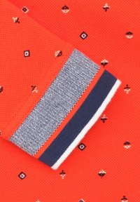 Rode textuurstof met kleine geometrische patronen en contrasterende marineblauwe en witte gestreepte manchetten. Accenten omvatten geborduurde details.