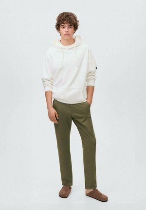 Vit huva sweatshirt med snörning, olivgröna byxor och bruna slip-on skor, mot en neutral bakgrund.