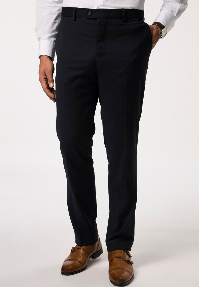 Pantalones navy hechos de una tela suave, con un diseño de frente plano, bolsillos laterales y pasadores para cinturón, combinados con zapatos de doble hebilla marrones.
