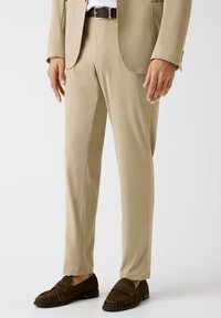 Beige pantalon van gladde stof, met een getailleerde snit, een platte voorkant en een slim fit. Gecombineerd met donkerbruine loafers.