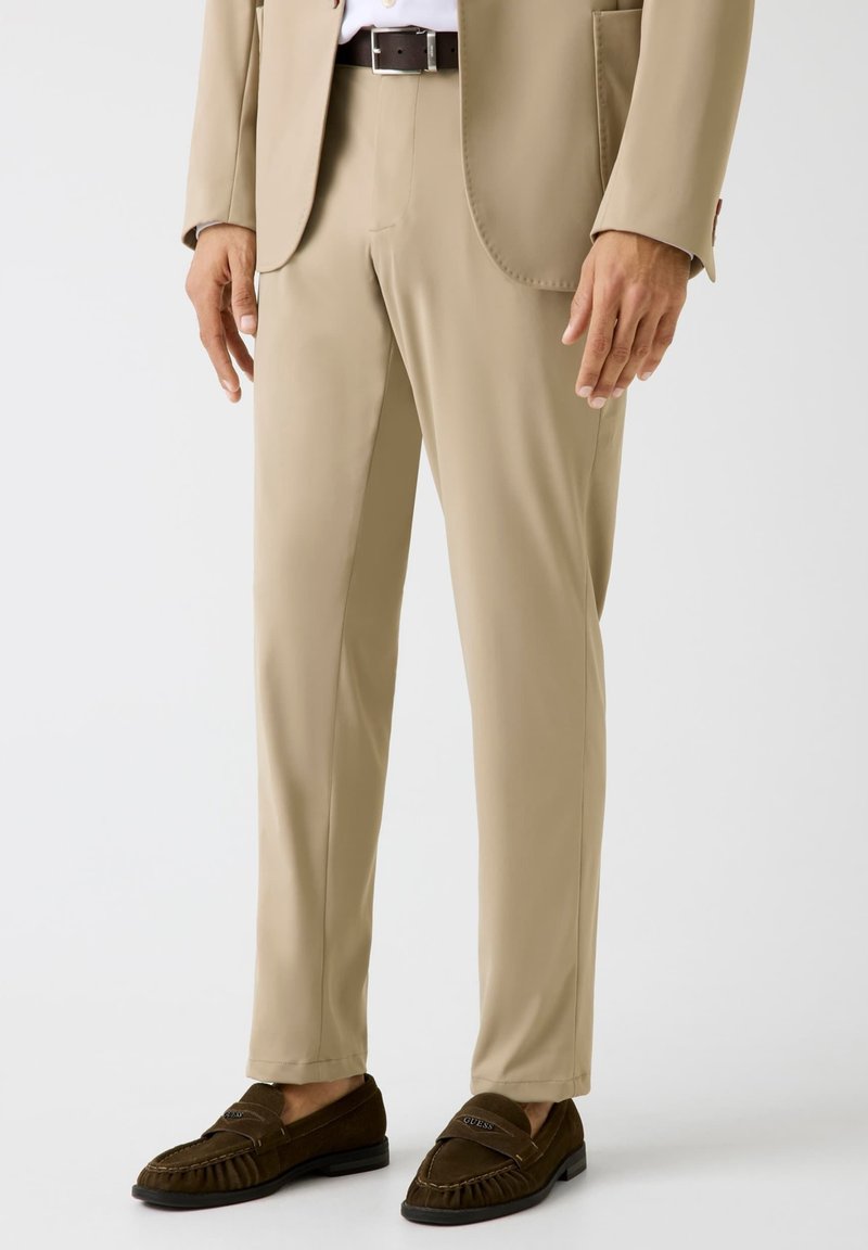 Beige pantalon van gladde stof, met een getailleerde snit, een platte voorkant en een slim fit. Gecombineerd met donkerbruine loafers.