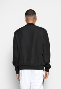 Giubbotto bomber nero in tessuto testurizzato, con polsini e orlo a coste, e colletto alto. Presenta un design semplice e slanciato, privo di decorazioni.
