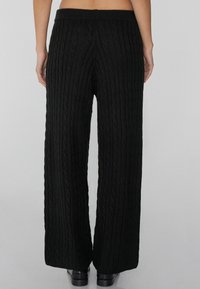 Zwarte kabelgebreide wijde broek met een textuurpatroon, voorzien van een elastische tailleband en een ontspannen pasvorm.