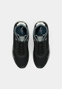 Zapatillas deportivas negras con parte superior de textil suave, cordones redondeados y una entresuela acolchada. Presentan detalles en gris y un logo en la lengüeta.