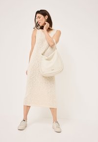 Abito di maglia crema lungo fino al ginocchio con un motivo texturizzato, abbinato a una borsa hobo in pelle bianca e sneaker chiare con dettagli sottili.