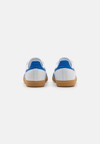 Hvite sneakers med blå accenter, med glatt overmateriale, teksturert bakside og såle i gummi. Flate snøringhull er inkludert.