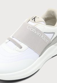 Άσπρο και ανοιχτό γκρι αθλητικό παπούτσι Calvin Klein με ελαστικό λουράκι στο πάνω μέρος και το ανάγλυφο λογότυπο CK στη γλώσσα.