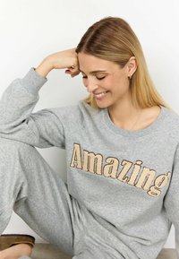 Szürke sportöltöny puha anyagból; a mellkason világosbarna betűkkel az "Amazing" felirattal. Laza szabású, bordázott mandzsettákkal.