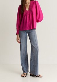 Blusa fucsia con bordo in pizzo e chiusura a bottoni, abbinata a jeans a gamba larga blu chiaro con dettagli di cucitura e orlo scolorito.