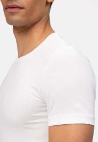 Weißes Kurzarm-T-Shirt aus einem glatten Baumwollgemisch. Hat einen runden Halsausschnitt und ein kleines gesticktes Logo am Ärmel.