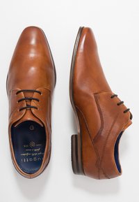 Chaussures habillées en cuir marron avec une texture lisse, design à lacets, bout arrondi et semelle foncée contrastante. L'intérieur présente un logo de marque.