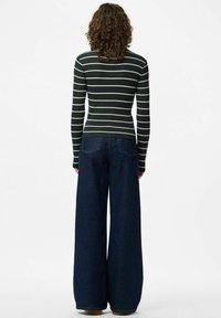 Svītrainā, ribotā džemperis tumši zaļā un krēmkrāsas tonī, pieguļoša silueta. Platā kāju tumšā denima bikses ar aizmugurējām kabatām, brīvi pieguļoša un strukturēta forma.