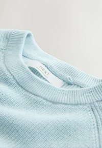 Világoskék pulóver, texturált felülettel, bordázott nyakkal és a "NEXT" feliratú címkével. Az anyag lágy és kötött hatású.
