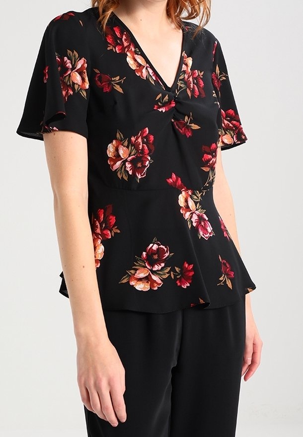 Blouse noire à manches courtes avec des imprimés floraux rouges, roses et orange, col en V et détail froncé torsadé au niveau de la poitrine.