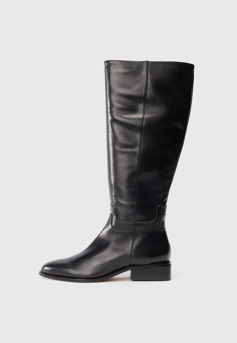 Bota de cuero negra hasta la rodilla con tacón bajo y punta redonda, fotografiada contra un fondo gris claro liso.
