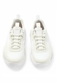 Bílé atletické tenisky s pleteným svrškem, texturovanou gumovou podrážkou, vrstveným designem a plochými tkaničkami. Logo je viditelné na jazyku a patě.