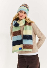 Wielobarwny wełniany szalik z paskami w kolorze niebieskim, zielonym, żółtym, brązowym i kremowym. Zawiera niebieską naszywkę dekoracyjną. Pasuje do dopasowanej czapki beanie.