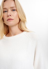 Maglione bianco e morbido con scollatura rotonda e maniche raglan. Presenta un tessuto testurizzato con una finitura liscia. Design semplice, senza fantasie o accenti.