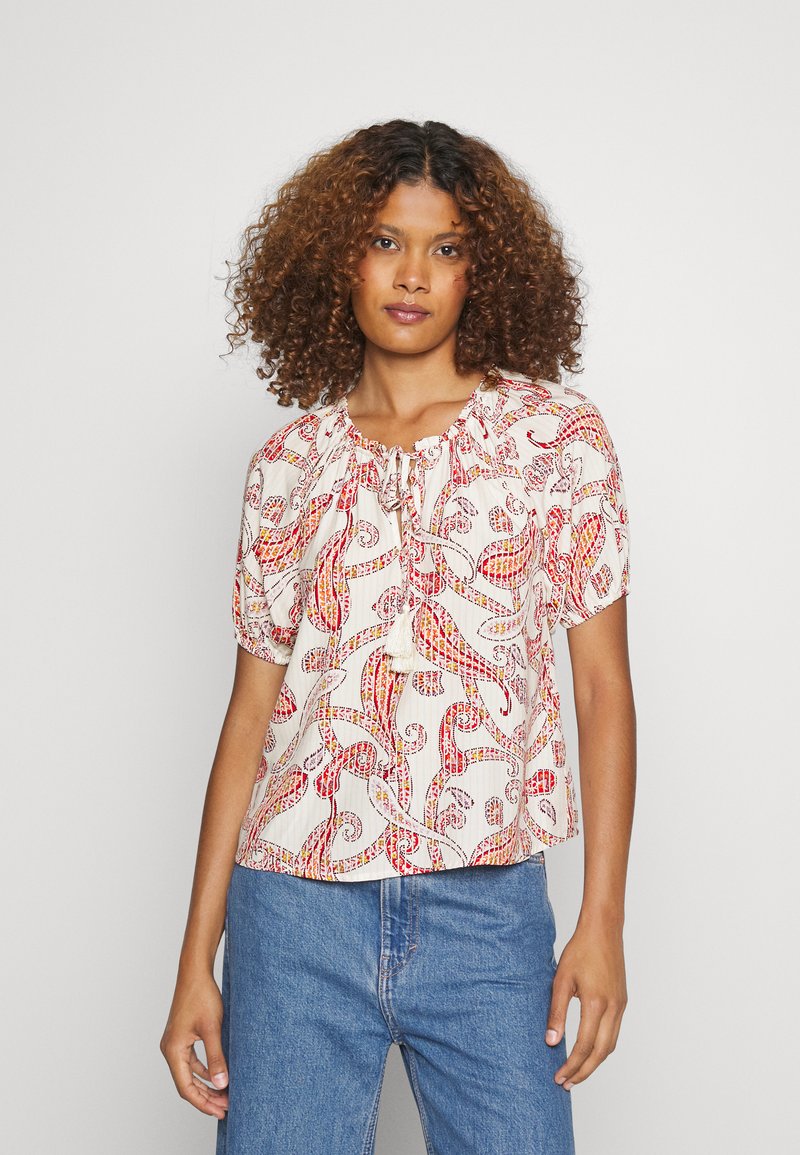 Blusa de mangas curtas em tecido leve e estampado com espirais em vermelho e amarelo. Apresenta um decote franzido e um detalhe laço na parte da frente.