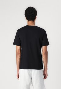 Svart bomull T-skjorte med korte ermer og rund hals, med en glatt tekstur og en avslappet passform bak, kombinert med lysegrå shorts.