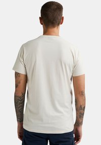 Cremefarvet bomulds T-shirt med korte ærmer, rund halsudskæring og en glat tekstur. Viser synlige tatoveringer på venstre arm.