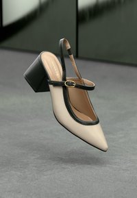 Beige pointed-toe slingback shoe with a black trim, featuring a block heel and a side buckle closure. Smooth finish with a minimalistic design.