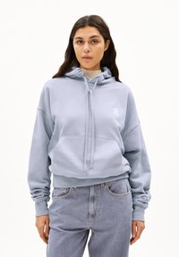 Lichtblauwe cropped hoodie met een trekkoord, een voorkantvak en een wit logo op de borst. Gemaakt van zachte, gestructureerde stof. In combinatie met lichtdenim jeans.