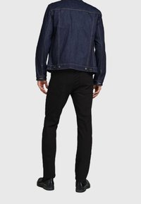 Chaqueta de mezclilla oscura con un corte clásico, que presenta un cuello puntiagudo, yugo trasero y cierre de botones; combinada con pantalones negros ajustados y zapatos negros.