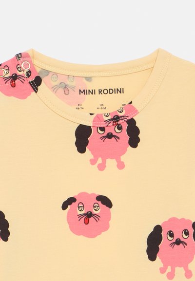 Žltý krátky rukáv top s hravými ružovými ilustráciami psov, okrúhlym výstrihom a detailom s patentkami. Mäkká textúra a ľahký materiál.