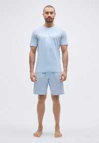 Ανοιχτό μπλε βαμβακερό T-shirt με την επιγραφή «ΚΟΥΡΑΣΜΕΝΟΣ» σε λευκό. Συνδυάζεται με αντίστοιχο ανοιχτό μπλε σορτς. Απλός, κοντομάνικος σχεδιασμός.