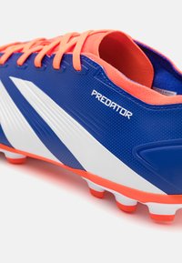 Botín de fútbol azul con parte superior texturizada, acentos blancos, cordones naranjas y suela roja. Logotipo "Predator" en el lateral.