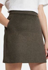 Gonna in misto lana marrone con taglio dritto, tasche laterali e una texture liscia, caratterizzata da una vita alta per una vestibilità strutturata.