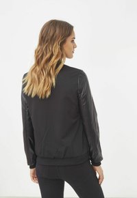 Chaqueta bomber negra con un cuerpo de tela suave y mangas de cuero brillante. El diseño se completa con puños y cintura de canalé. Sin patrones ni acentos.