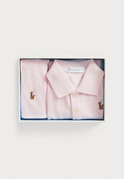 Polo rosa e botões de punho a condizer numa caixa, com um pequeno logótipo bordado de um cavalo, tecido leve e detalhe de abotoadura.