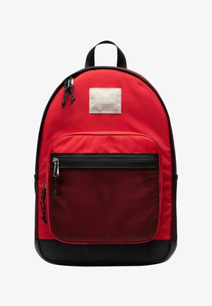 Mochila Herschel en rojo y negro con un bolsillo frontal de malla con cremallera, dos deslizadores de cremallera y una asa superior para llevar.