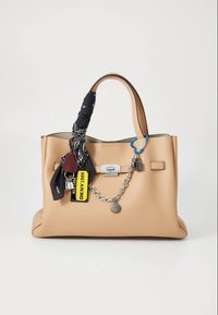 Beige läderväska med kedjedetalj, en nyckelring och en mönstrad sjal knuten runt handtaget. Har silverfärgade metallbeslag och märkesetiketter.