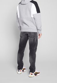 Felpa grigia con dettagli bianchi e neri, abbinata a jeans neri sbiaditi e sneaker colorate con dettagli gialli e rossi.