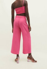 Haut court rose à design smocké avec bretelles fines, associé à un pantalon rose à jambes larges et des sandales à talons blocs à brides.