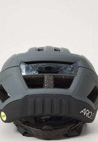Grau Fahrradhelm mit strukturierter Oberfläche, großen Lüftungsschlitzen und einem reflektierenden Visier. Verfügt über einen Aufkleber mit MIPS-Technologie an der Seite.