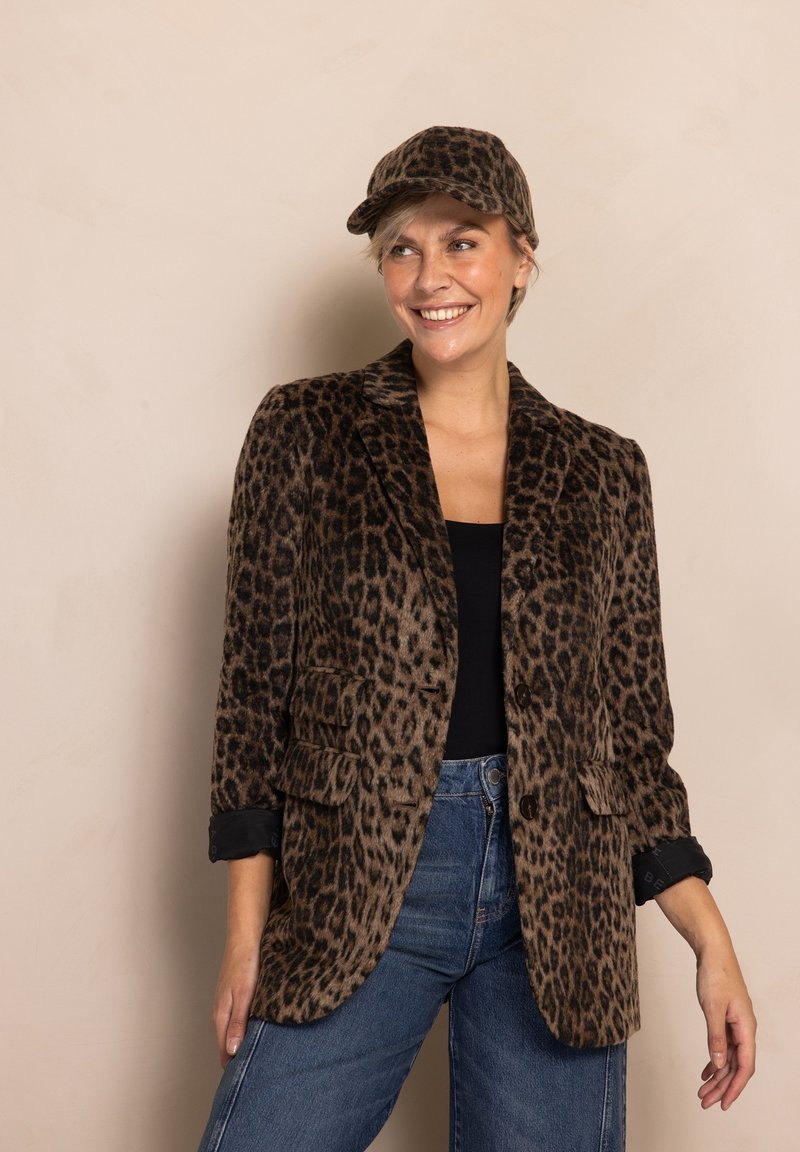 Blazer mit Leopardenmuster in strukturierter Stoffqualität, ausgestattet mit zwei Fronttaschen, hochgekrempelten Ärmeln und klassischem Revers, kombiniert mit einer passenden Kappe.