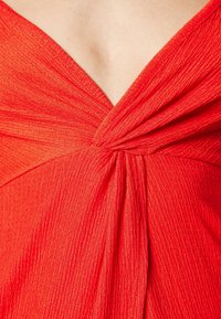 Gros plan sur un tissu rouge vif texturé, torsadé en un décolleté en forme de V sur un vêtement.