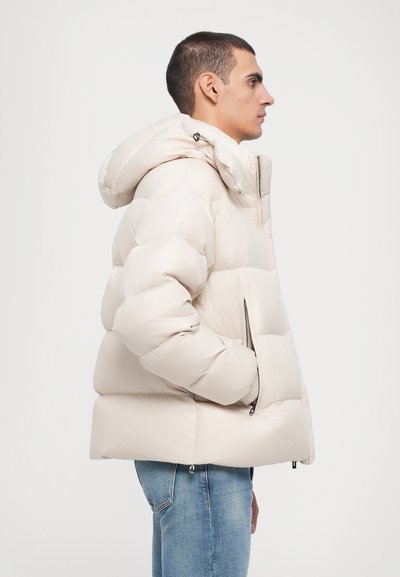 Puffjakke i lys beige med hætte, med et quiltet design, frontlynlås og sidelommer. Blød tekstur og voluminøs form.